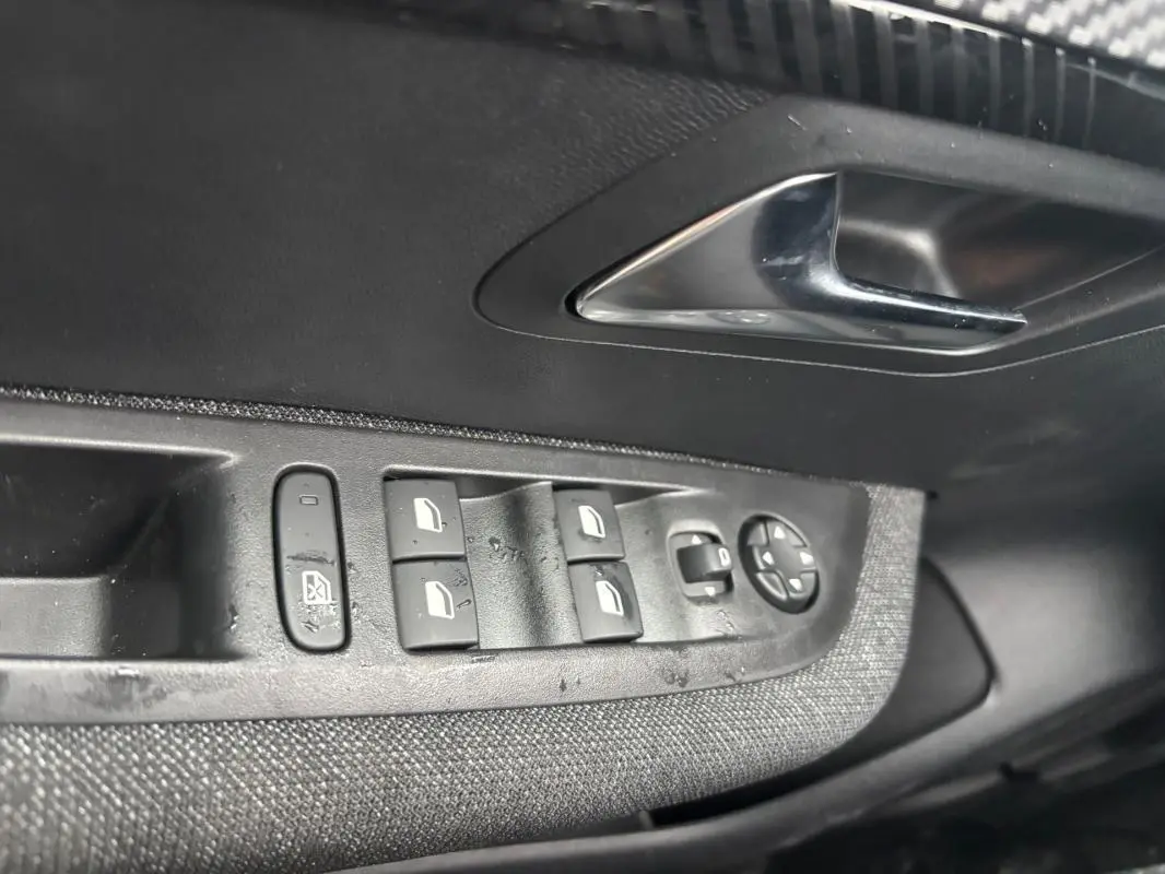 Gros plan sur les commandes des vitres électriques et rétroviseurs côté conducteur d'une Peugeot 208 Hybrid 100 e-DCS6 Style gris 2025.