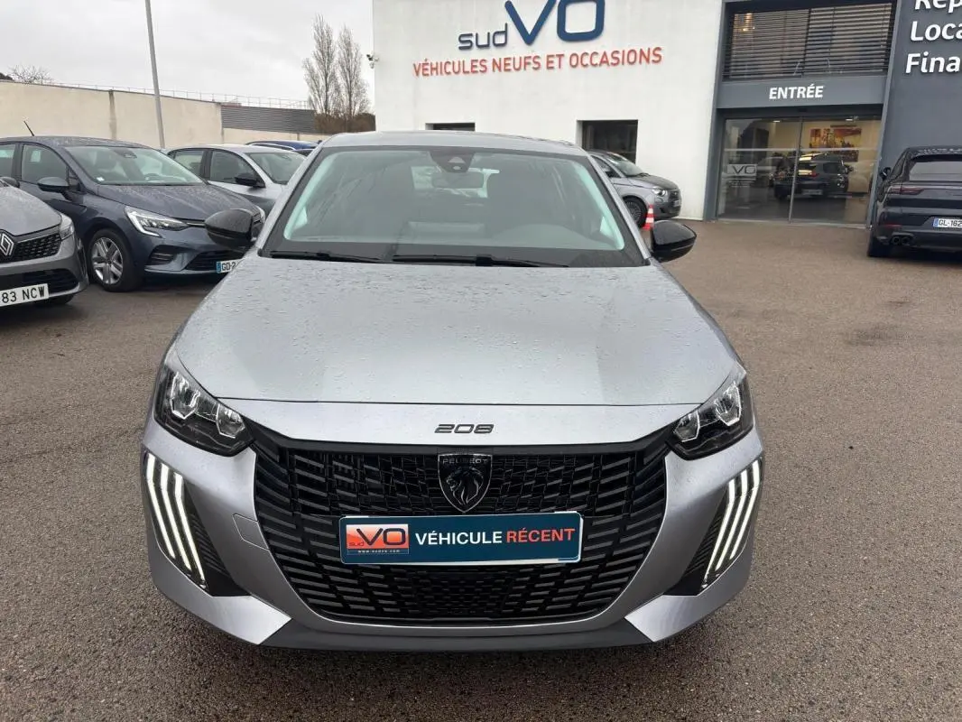 Vue avant d'une Peugeot 208 Hybrid gris métallisé avec feux diurnes LED en forme de griffes, stationnée devant un concessionnaire.