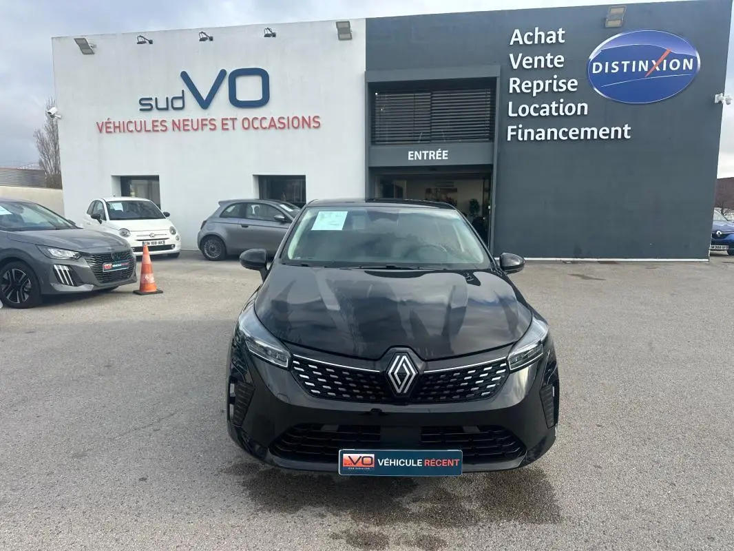 Vue avant d'une Renault Clio V dCi 100 Evolution noire stationnée devant un concessionnaire avec logo Renault visible.