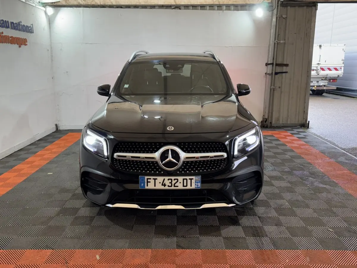 Vue avant d’un Mercedes GLB 200 d AMG Line noir avec phares LED allumés dans un garage.