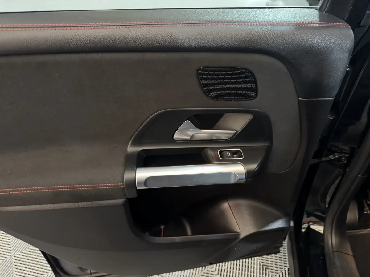 Gros plan sur la porte intérieure côté gauche noire du Mercedes GLB 200 d AMG Line avec surpiqûres rouges et poignée alu.
