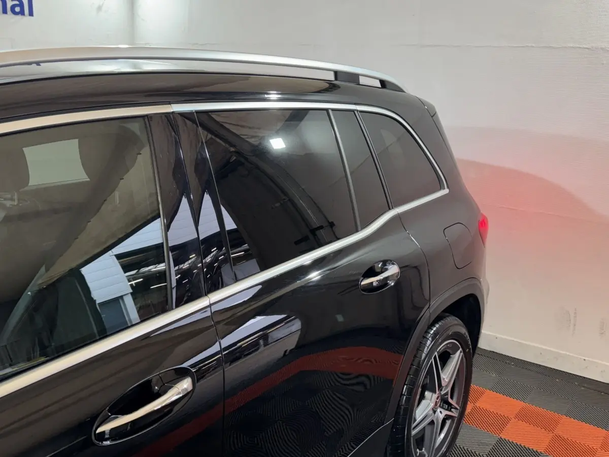 Vue latérale arrière droite d’un Mercedes GLB 200 d AMG Line noir avec jantes alliage et barres de toit chromées.