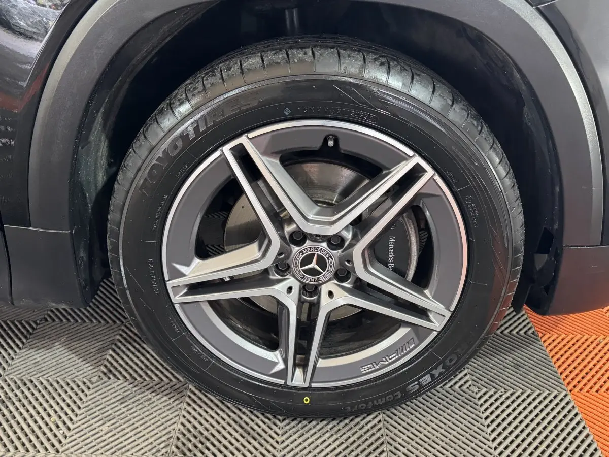 Gros plan sur la roue avant droite noire du Mercedes GLB 200 d AMG Line avec jante AMG à cinq branches.