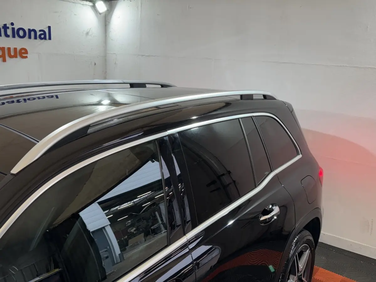 Vue 3/4 arrière droite du Mercedes GLB 200 d AMG Line noir avec barres de toit chromées et vitres teintées.