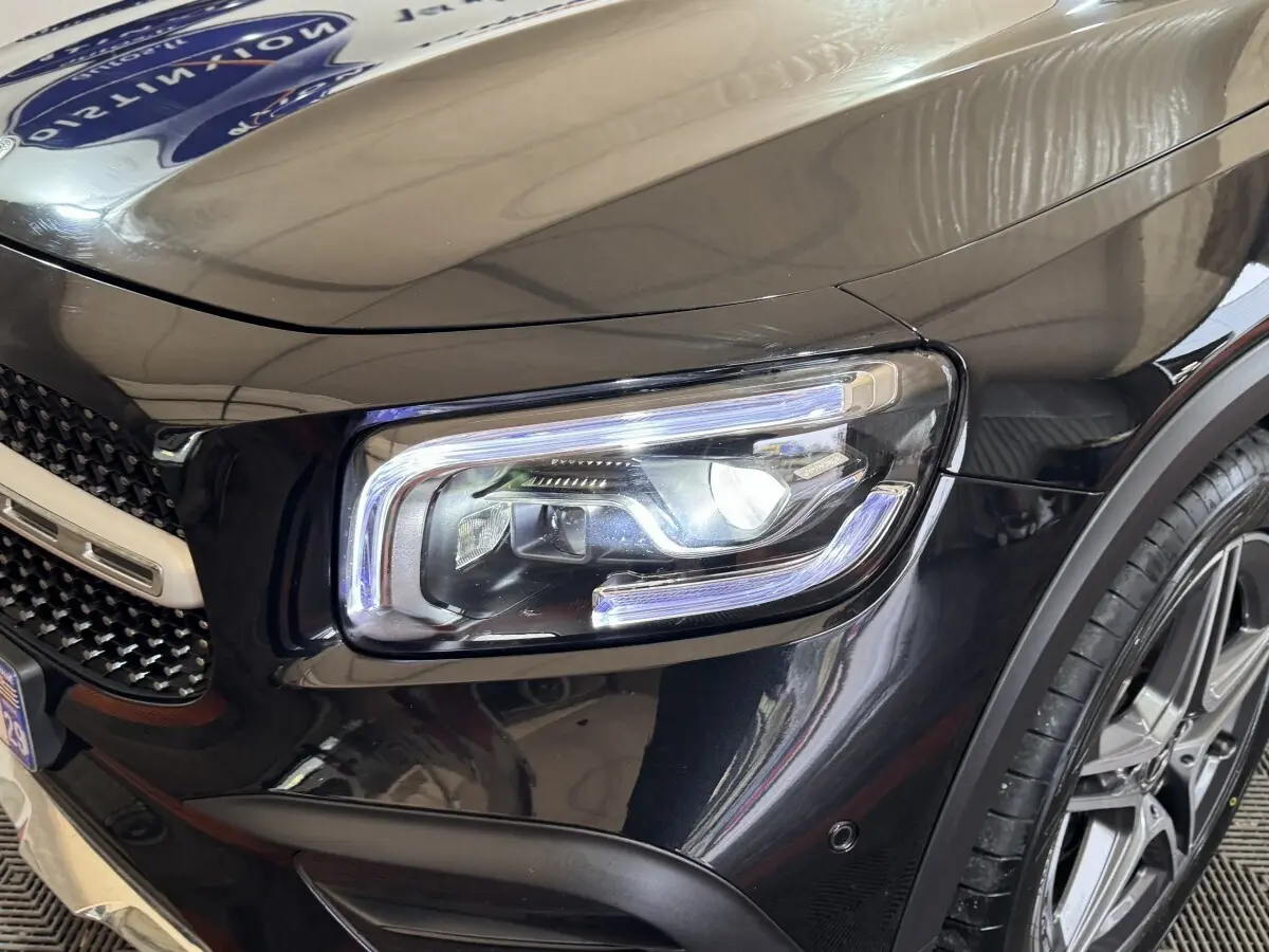 Gros plan sur le phare avant droit du Mercedes GLB 200 d AMG Line noir, avec jante alliage visible et calandre partielle.