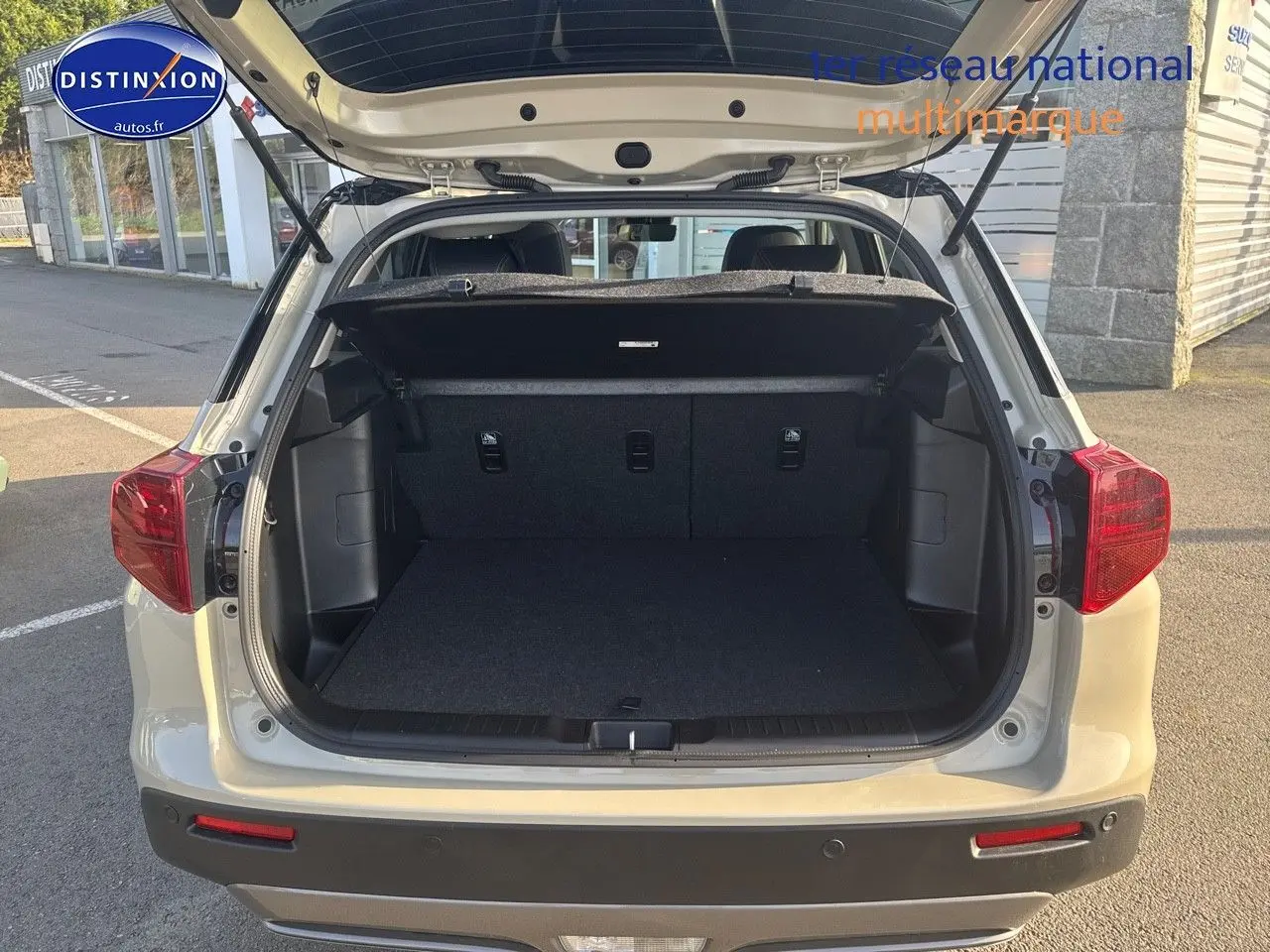 Vue arrière du Suzuki Vitara 1.4 Boosterjet Hybrid 2026 en So'Color Savanna Ivory avec coffre ouvert et hayon relevé.