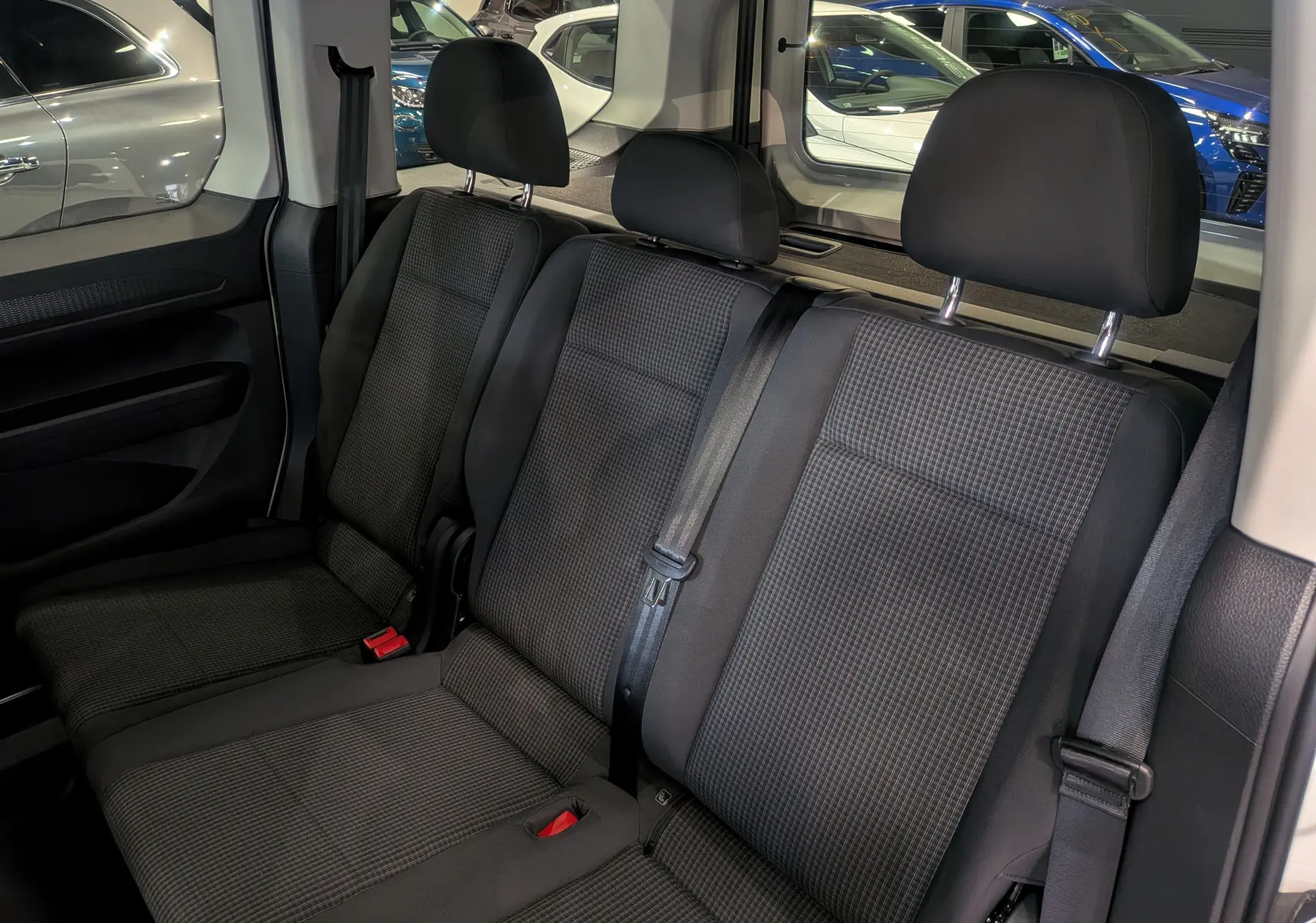 Vue intérieure des sièges arrière en tissu noir du Volkswagen Caddy 2.0 TDI 2025, avec ceintures de sécurité visibles.