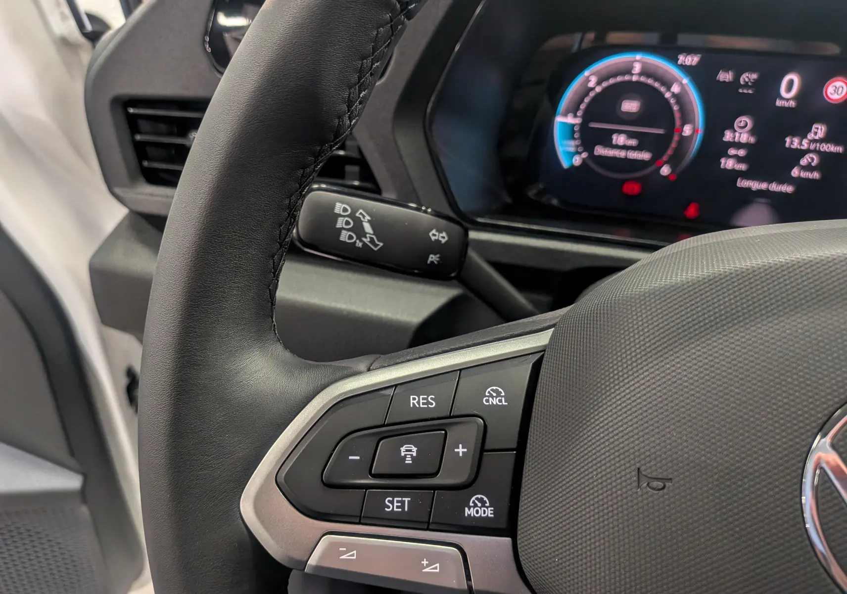 Gros plan sur le volant noir du Volkswagen Caddy blanc 2025, avec commandes de régulateur de vitesse et tableau de bord numérique.