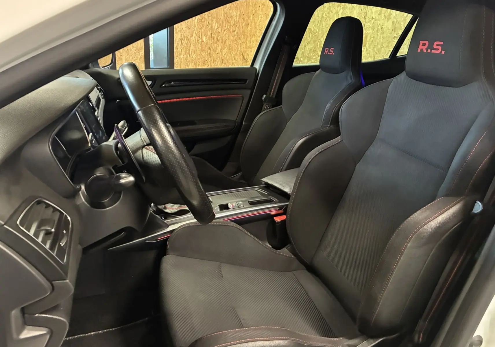 Vue intérieure côté conducteur de la Renault Mégane IV RS 280 EDC6 avec sièges sport noirs marqués R.S. en rouge.