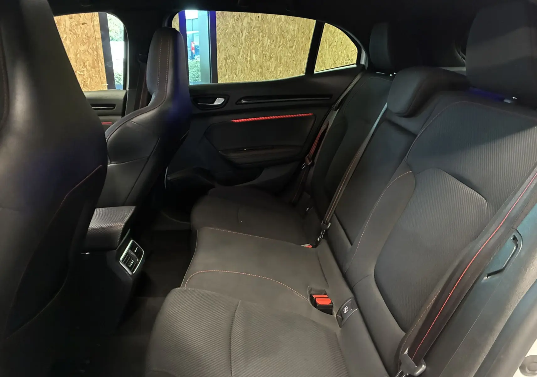 Vue intérieure arrière droite de la Renault Mégane IV RS 280 EDC6 avec sièges noirs et surpiqûres rouges.