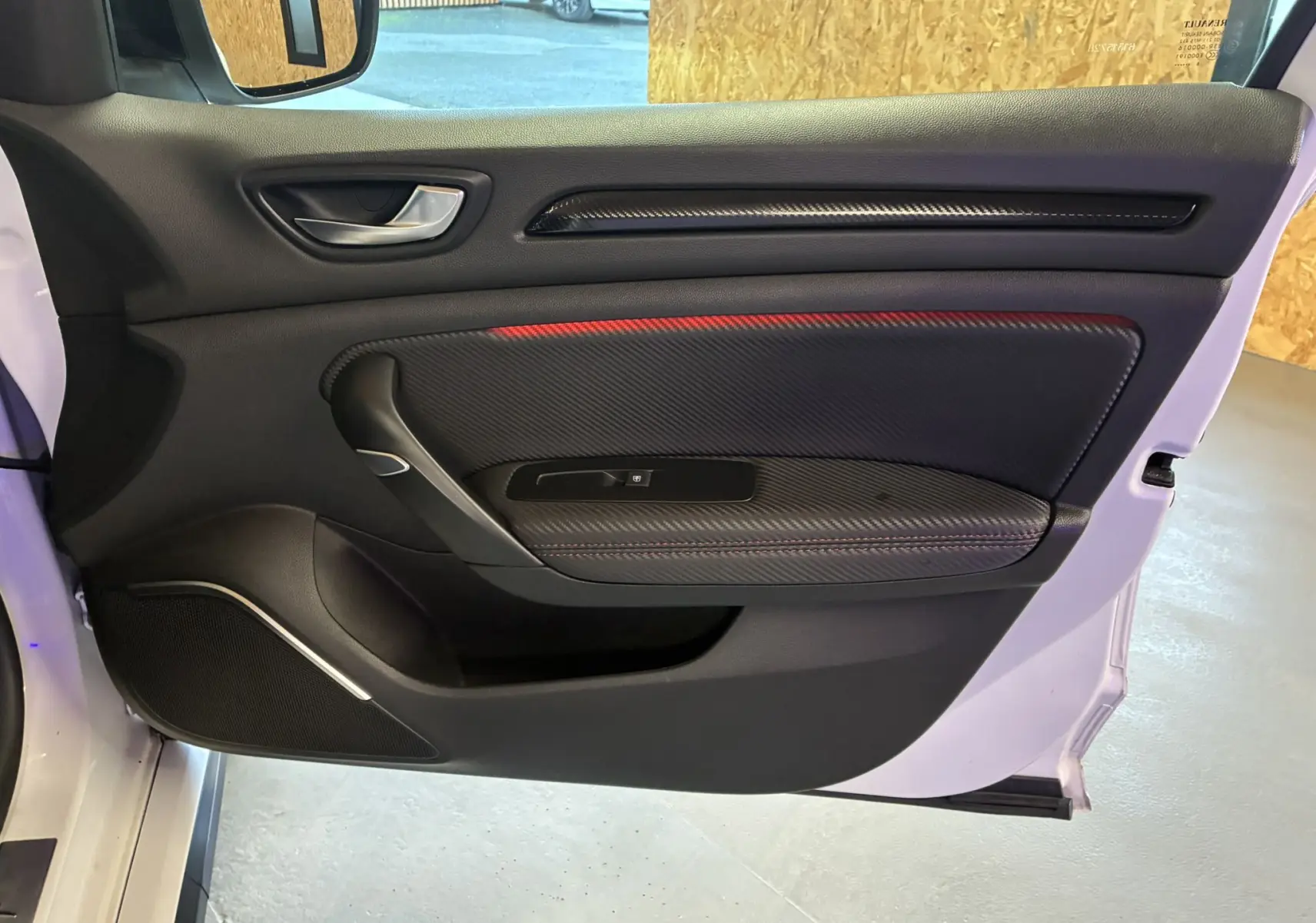 Vue intérieure de la porte avant gauche de la Renault Mégane IV RS 280 EDC6 blanche, avec garniture noire et surpiqûres rouges.