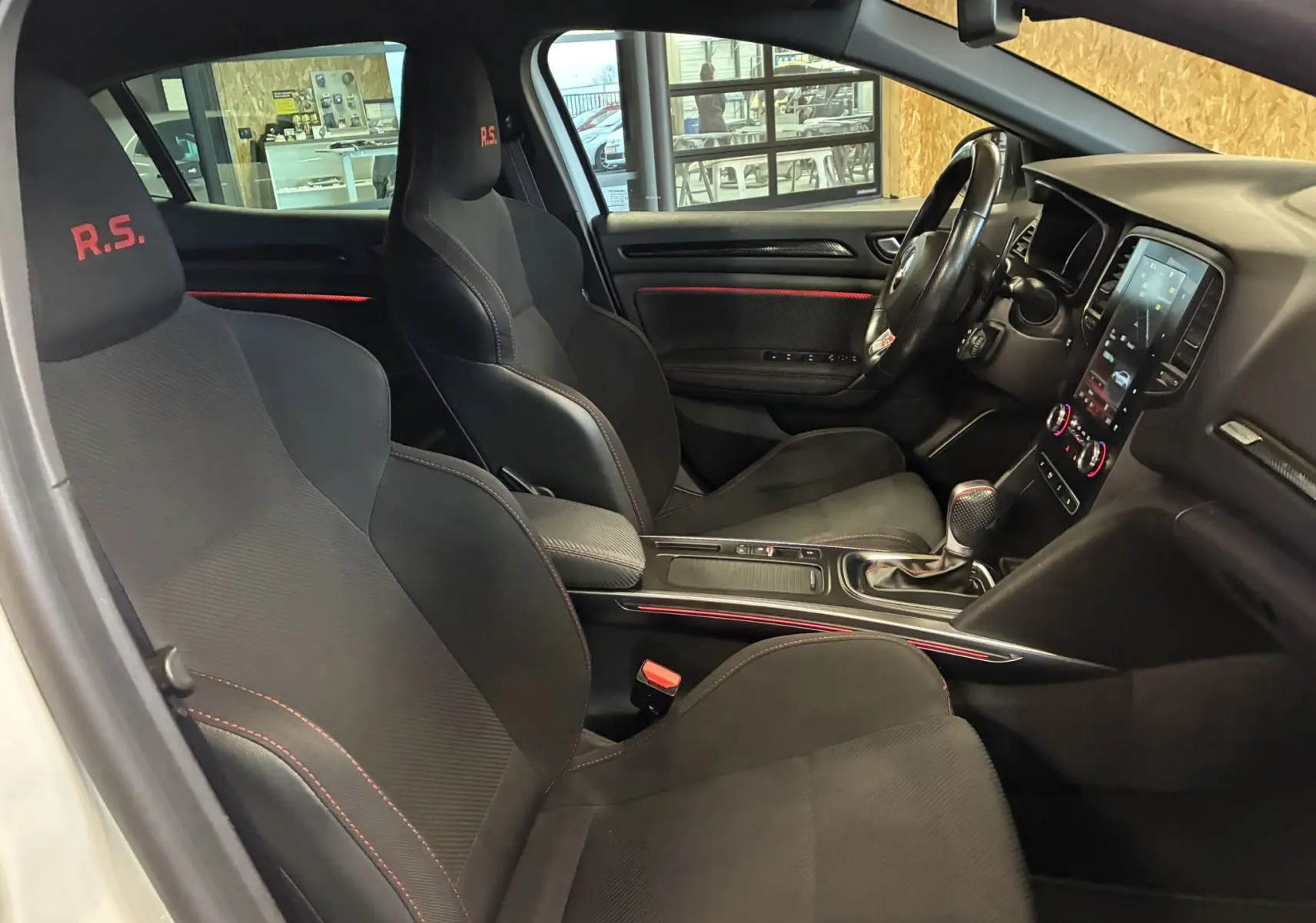 Vue intérieure côté conducteur de la Renault Mégane IV RS 280 EDC6 avec sièges noirs marqués R.S. et détails rouges.