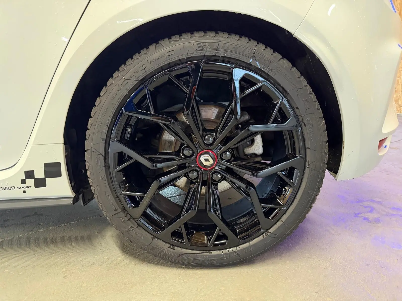 Gros plan sur la roue arrière droite noire brillante d'une Renault Mégane IV RS 280 blanche avec logo Renault rouge.