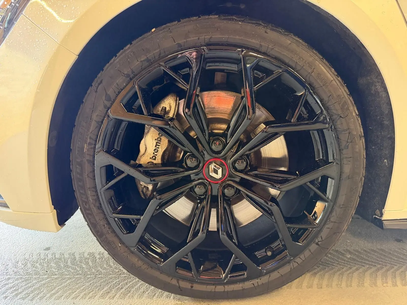 Gros plan sur la jante noire brillante de la Renault Mégane IV RS 280 EDC6 blanche avec logo Renault au centre.