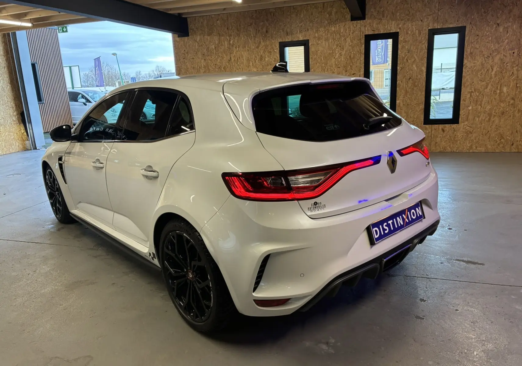 Vue 3/4 arrière droite d'une Renault Mégane IV RS 280 EDC6 blanche avec jantes noires dans un garage.