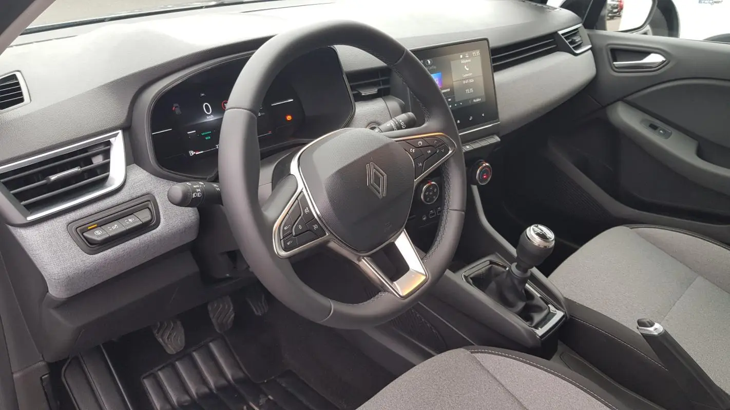 Vue intérieure côté conducteur de la Renault Clio gris 2025 avec volant multifonction et boîte manuelle.