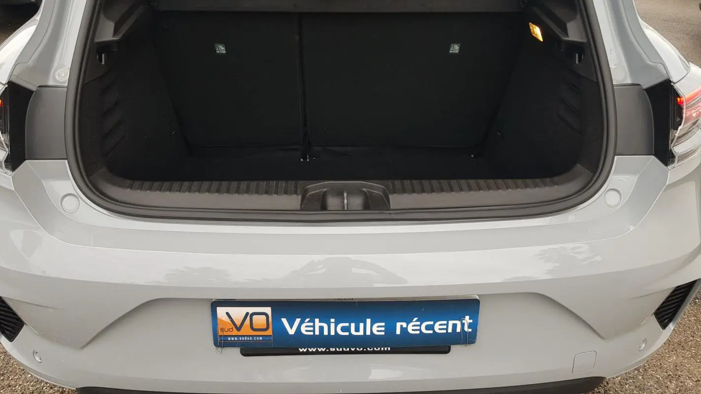 Vue arrière du coffre ouvert d'une Renault Clio gris clair, avec feux arrière et pare-chocs visibles.