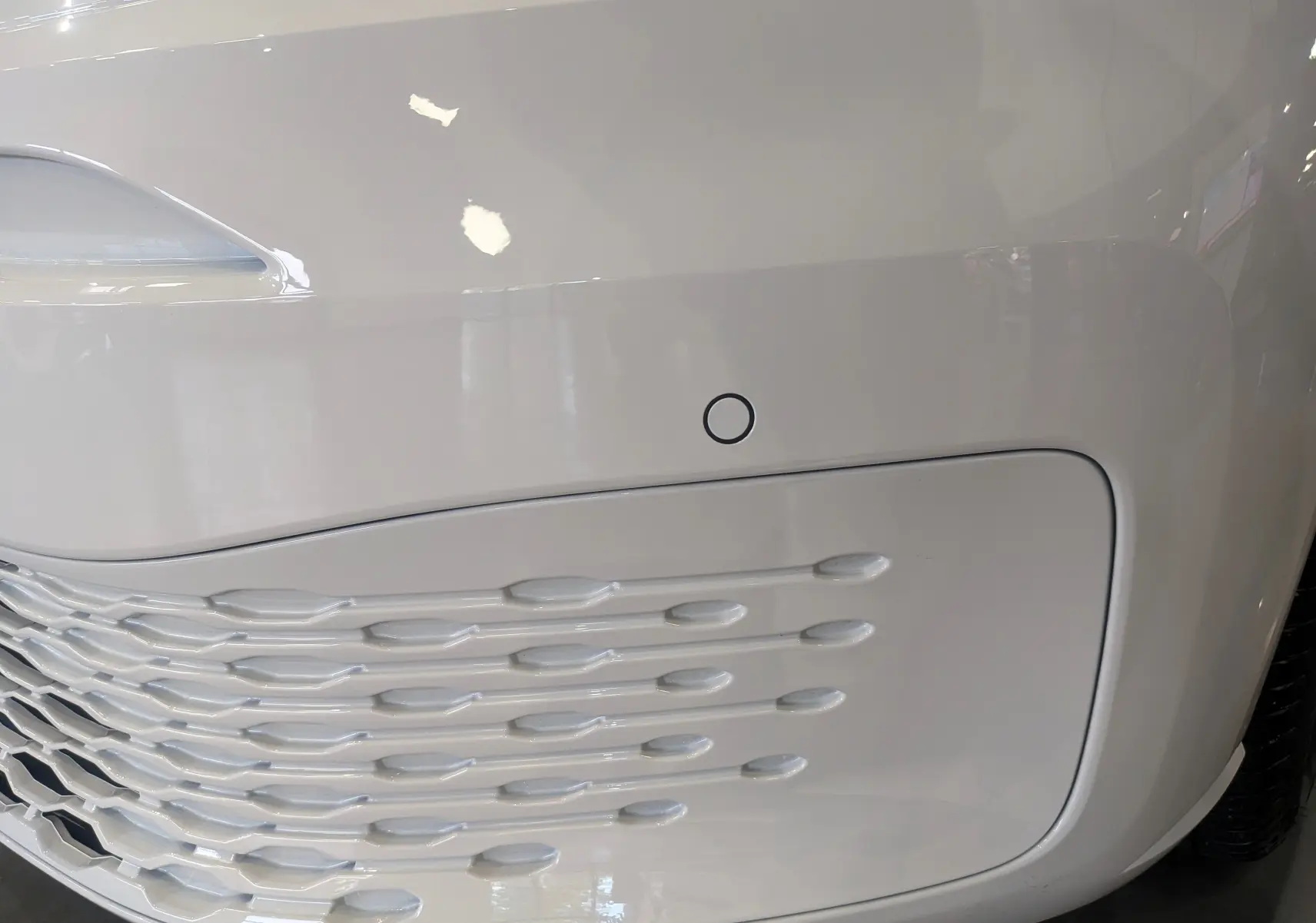 Détail du pare-chocs avant blanc du Volkswagen Caddy 2.0 TDI 102 CH 2025 avec capteur de stationnement intégré.