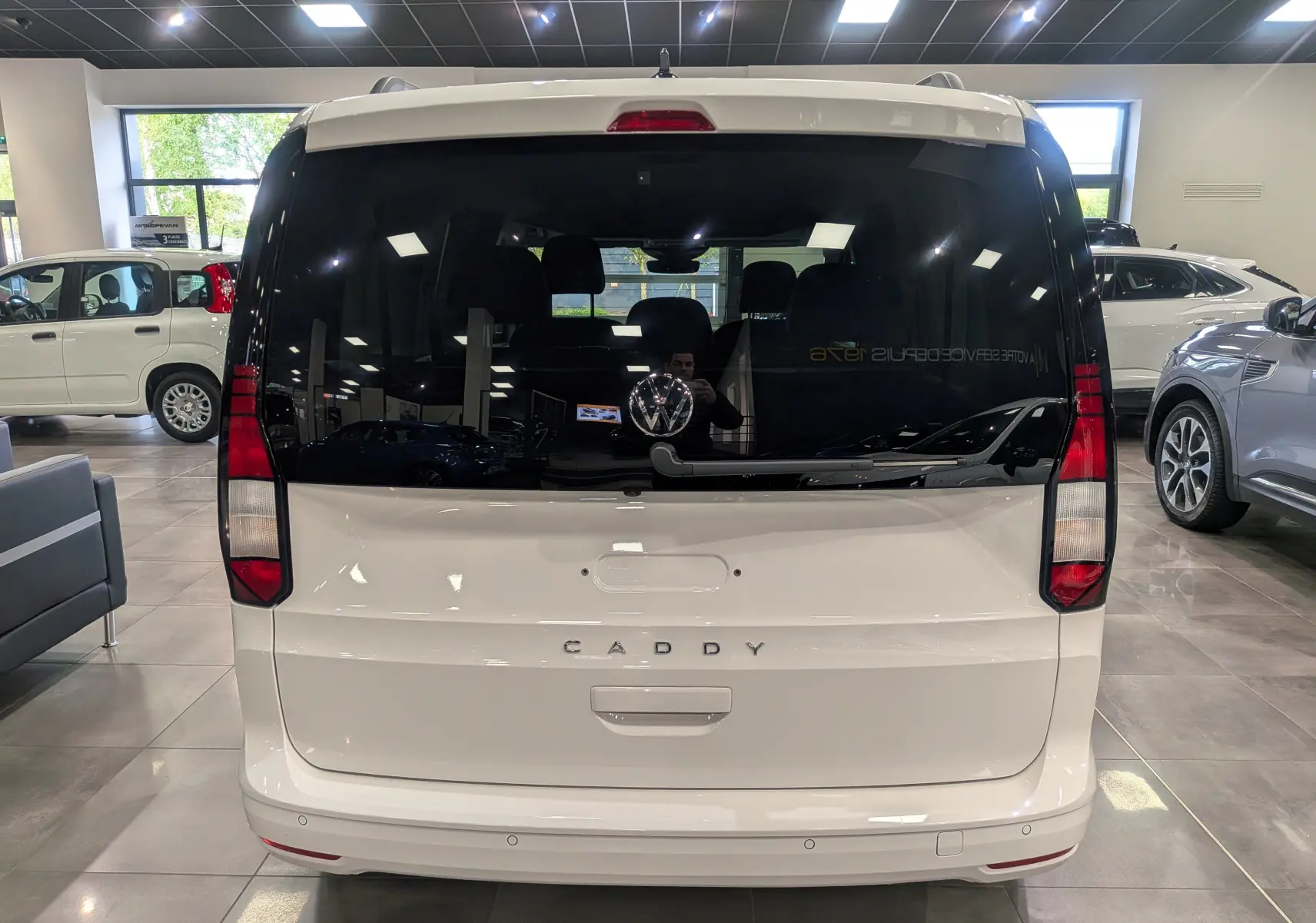Vue arrière d'un Volkswagen Caddy blanc 2025 avec vitres arrière teintées et logo VW visible au centre.