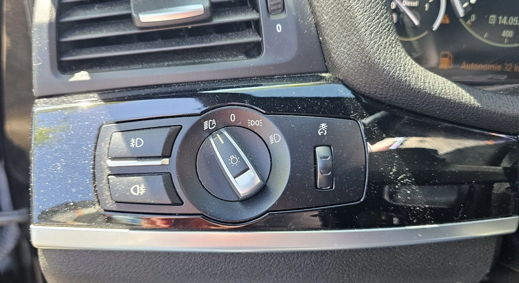 Gros plan sur le bouton de commande des phares sur tableau de bord noir brillant d'une BMW X4 xDrive20dA 2015.