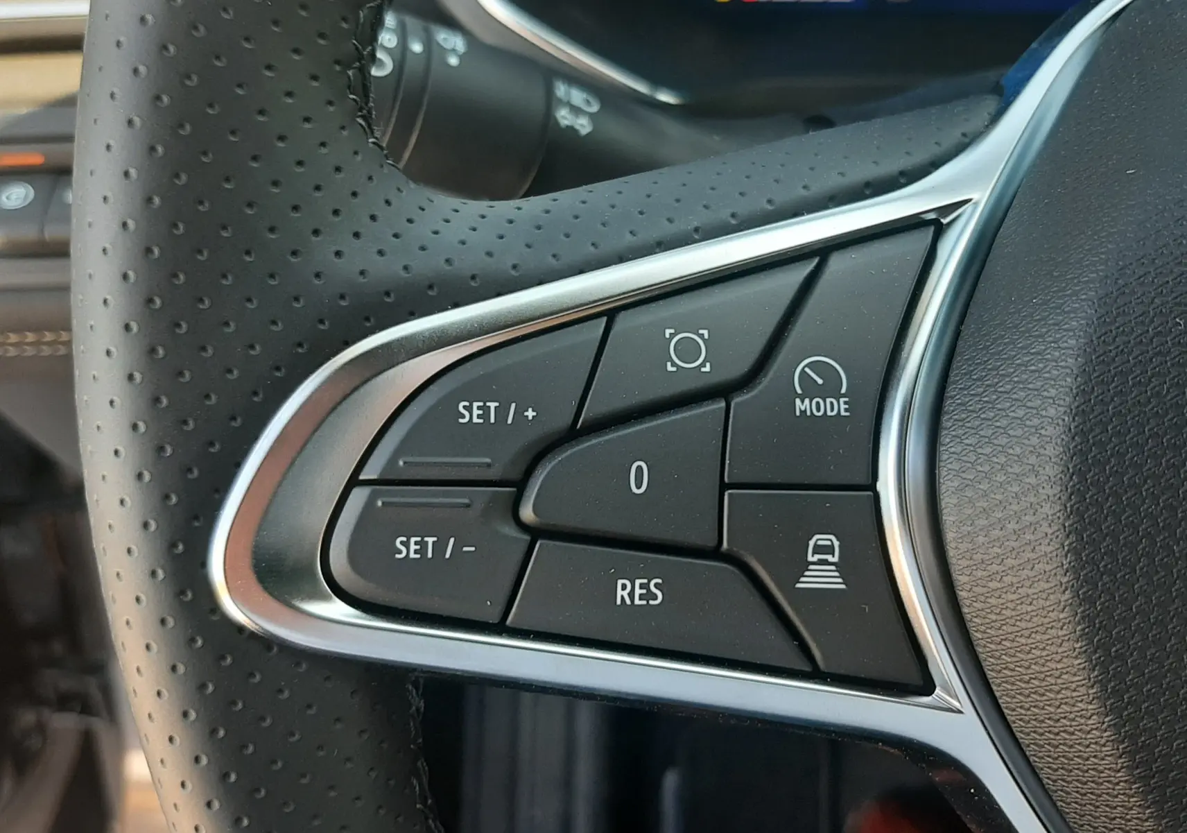 Gros plan sur les commandes de régulateur de vitesse au volant en cuir perforé noir du Renault Symbioz hybride.
