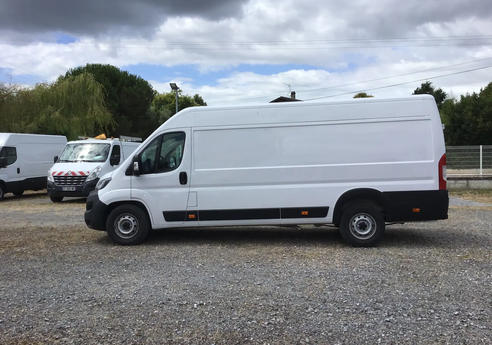 Fourgon blanc FIAT Ducato XLH2 3T5 vu de profil côté gauche sur un terrain gravillonné, sans marquages visibles.