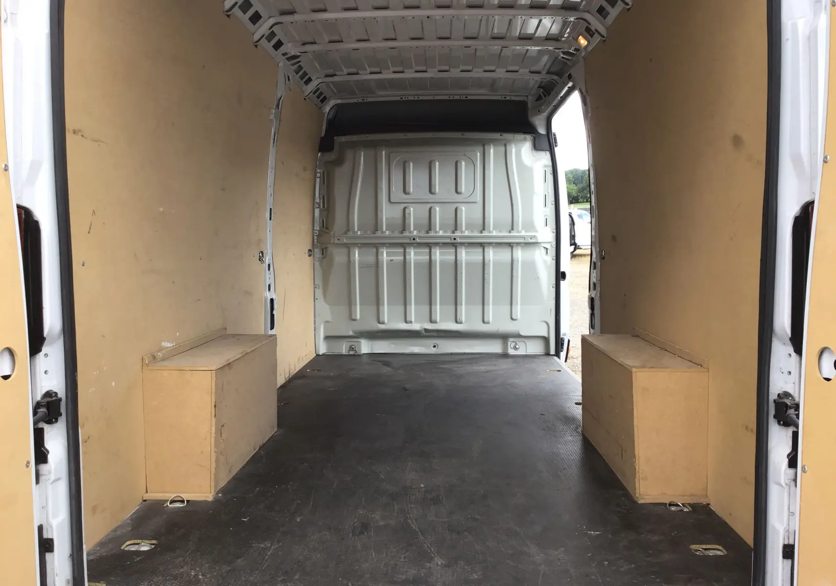 Intérieur du fourgon FIAT Ducato XLH2 blanc, vue de l'arrière avec parois et coffres en bois clair.