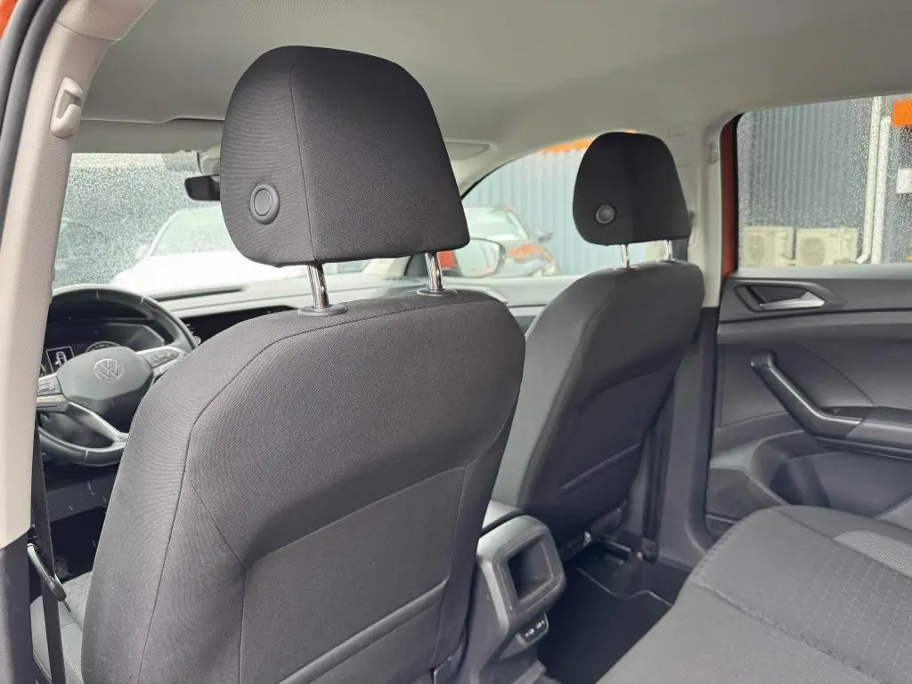 Vue intérieure arrière du Volkswagen T-Cross orange 2021, montrant les sièges avant en tissu noir et la console centrale.