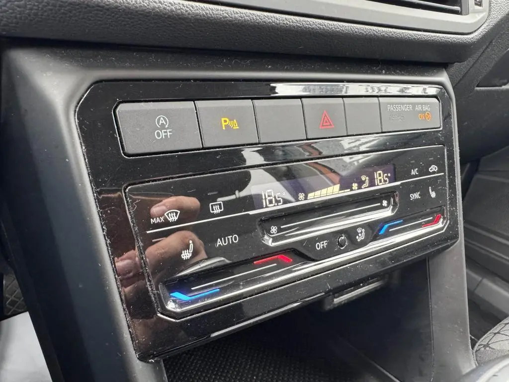 Gros plan sur la console centrale noire du Volkswagen T-cross 1.0 TSI Active, montrant les commandes de climatisation digitale et alertes.