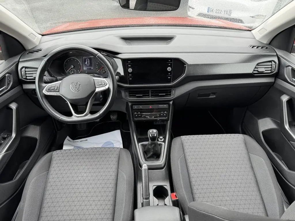 Vue intérieure avant du Volkswagen T-Cross 1.0 TSI 110 Active 2021, tableau de bord noir avec volant cuir et levier de vitesses manuel.