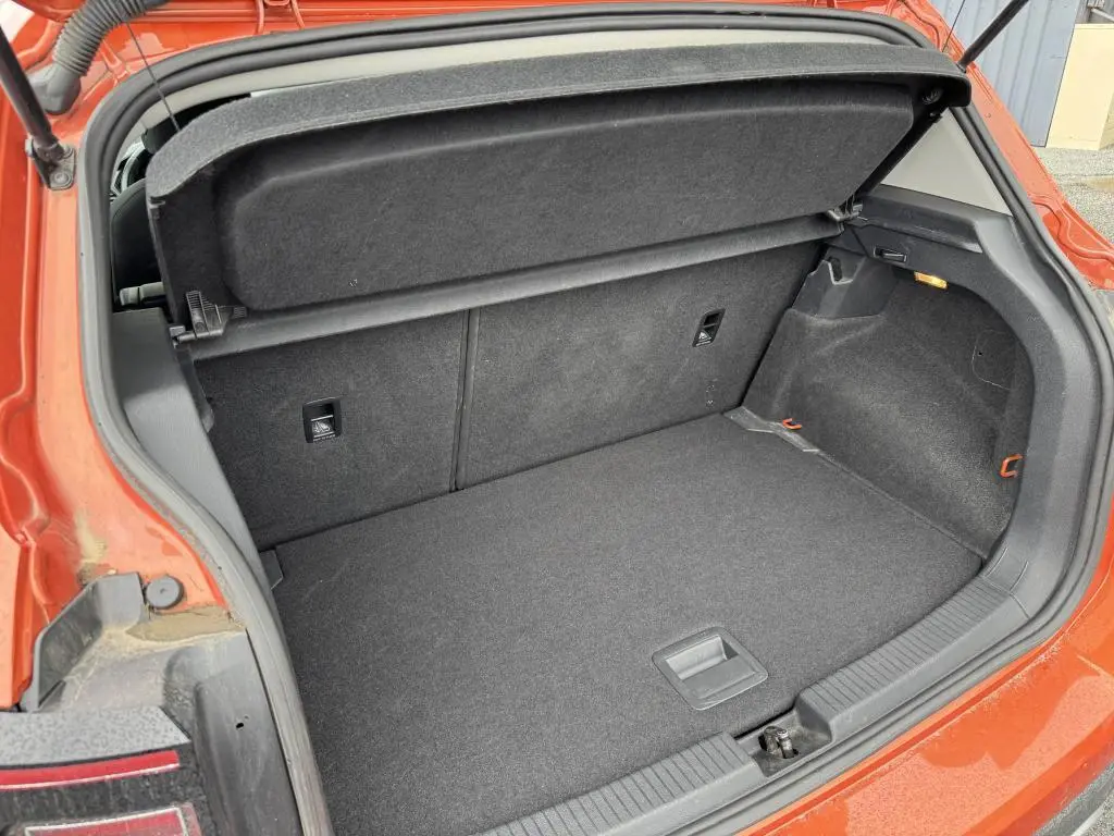 Coffre ouvert vu de l'arrière du Volkswagen T-Cross orange métallisé, montrant l'espace de chargement et la plage arrière.