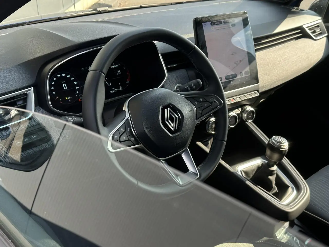 Vue intérieure du poste de conduite de la Renault Clio TCE 90 Techno 2025 avec volant multifonction et écran tactile vertical.