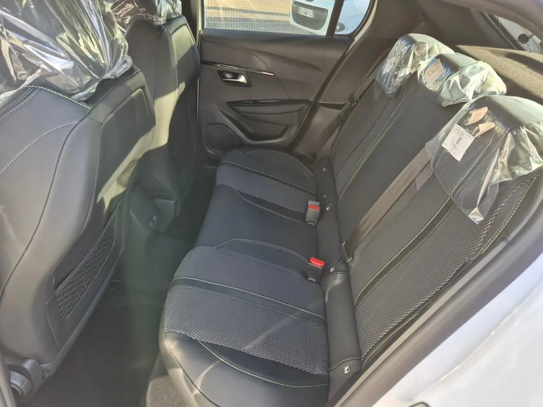 Vue intérieure arrière côté droit montrant les sièges noirs avec surpiqûres vertes d'une Peugeot 208 Hybrid 136 e-DCS6 GT blanche.