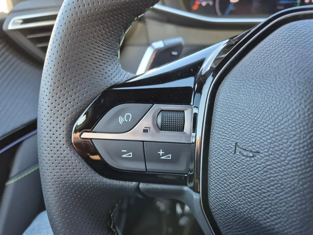 Gros plan sur le côté gauche du volant perforé noir de la Peugeot 208 Hybrid 136 e-DCS6 GT avec commandes audio intégrées.