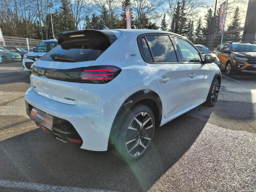 Vue 3/4 arrière droite d'une Peugeot 208 Hybrid 136 GT blanche avec jantes alliage 17 pouces et feux arrière LED distinctifs.