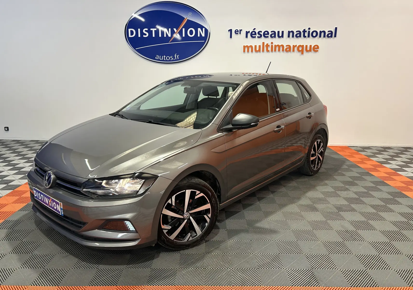 Volkswagen Polo gris vue 3/4 avant droit dans un showroom avec jantes noires et argentées.