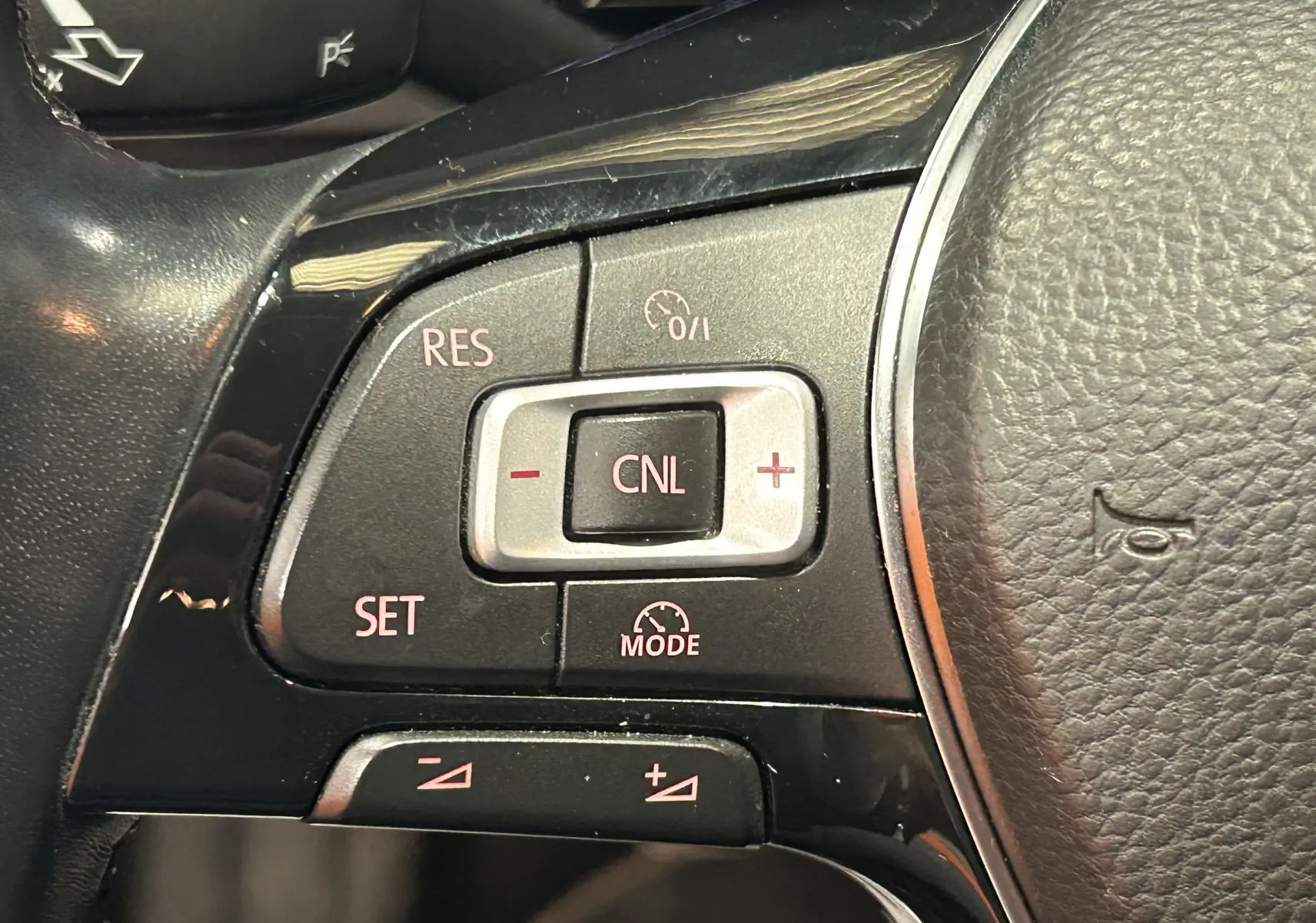 Gros plan sur les commandes de régulateur de vitesse à gauche du volant en cuir noir d’une Volkswagen Polo gris 2018.