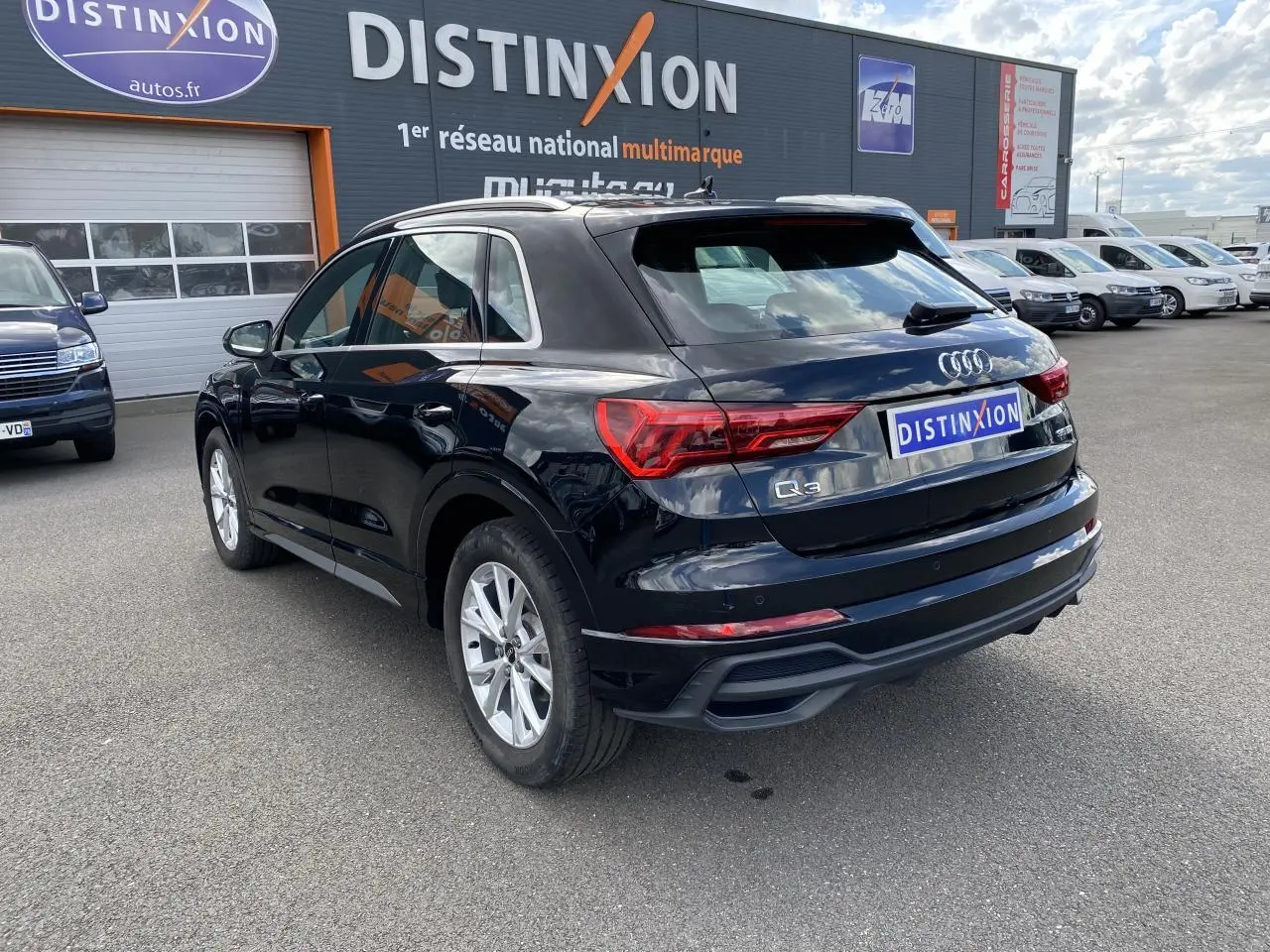 Audi Q3 noir intense métallisé vue 3/4 arrière droit, avec jantes aluminium et logo S line sur ailes avant.