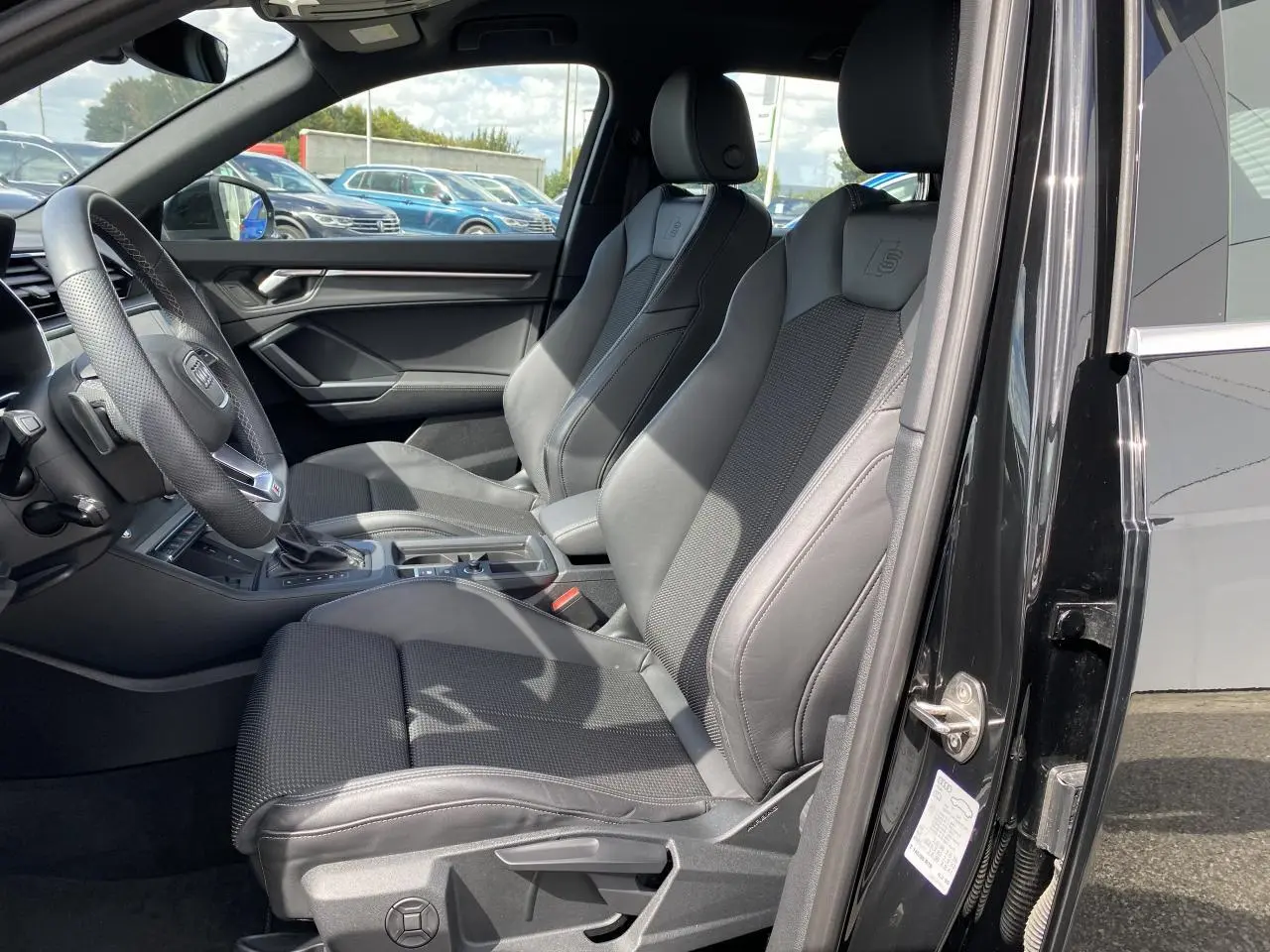 Vue intérieure côté conducteur de l'Audi Q3 S line 2024 avec sièges sport noirs et volant cuir multifonction.