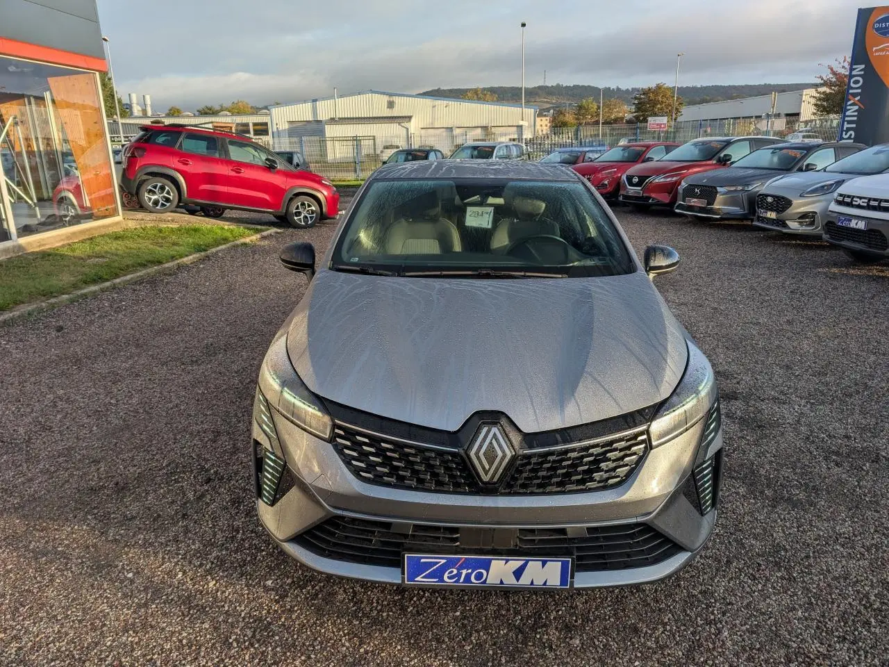 Renault Clio 2025 gris schiste vue de face, avec calandre noire et phares LED distinctifs, sur parking extérieur.