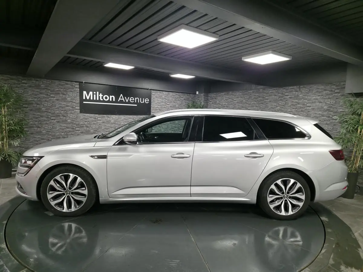 Profil côté gauche de la Renault Talisman Estate gris platine 2018 dans un showroom avec éclairage moderne.