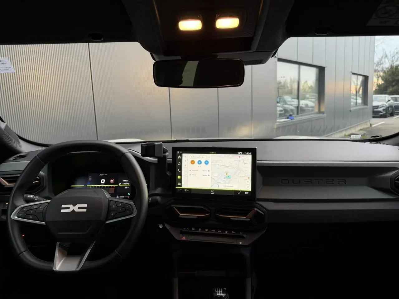 Vue intérieure avant du Dacia Duster 2025 beige Sandstone, tableau de bord digital et écran tactile central avec navigation.