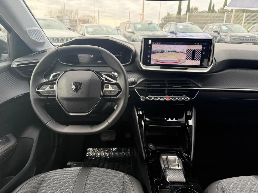 Vue intérieure avant du Peugeot 208 gris 2025, volant multifonction et écran tactile affichant la caméra de recul.