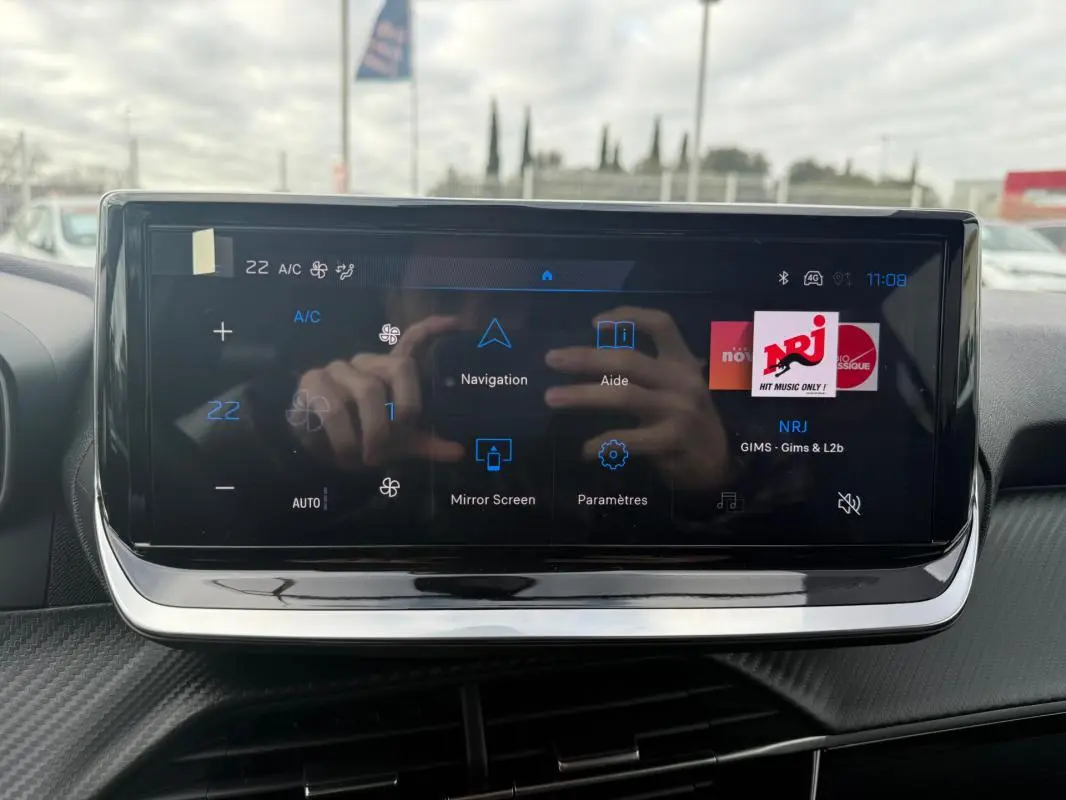 Écran tactile central du tableau de bord de la Peugeot 208 gris, affichant les options de navigation et radio NRJ.