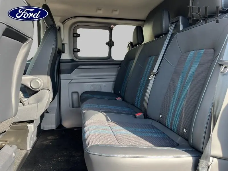 Vue intérieure du Ford Transit Custom Fourgon 2026, banquette arrière en tissu noir avec bandes bleues et ceintures de sécurité.