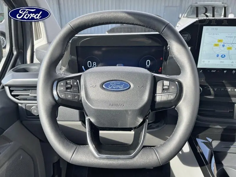 Vue rapprochée du volant noir du Ford Transit Custom 2026 avec tableau de bord numérique et écran tactile.