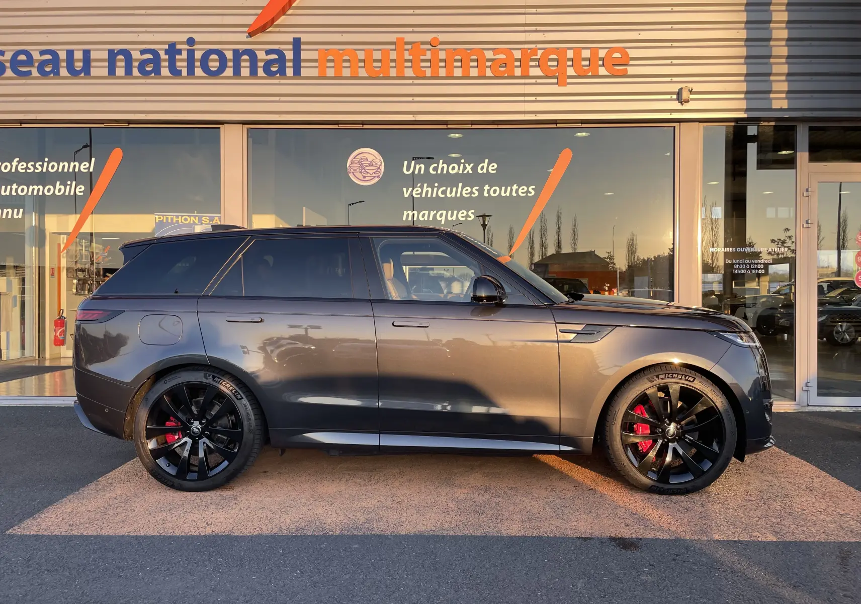 Vue de profil côté gauche d’un Range Rover Sport P440 HSE R-Dynamic gris Carpathian avec jantes noires 23'' et étriers de frein rouges.