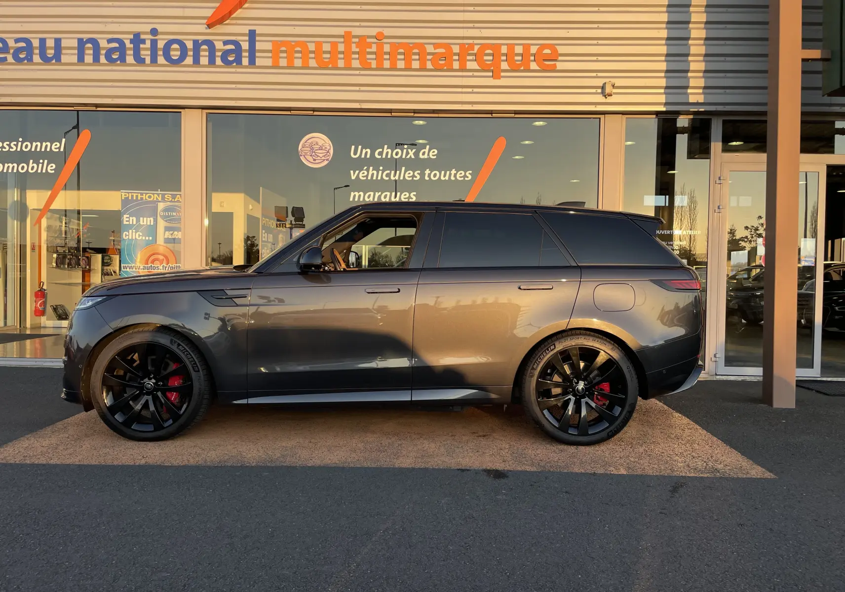 Vue de profil côté gauche d'un Range Rover Sport P440 HSE R-Dynamic gris Carpathian avec jantes noires 23'' et étriers rouges.