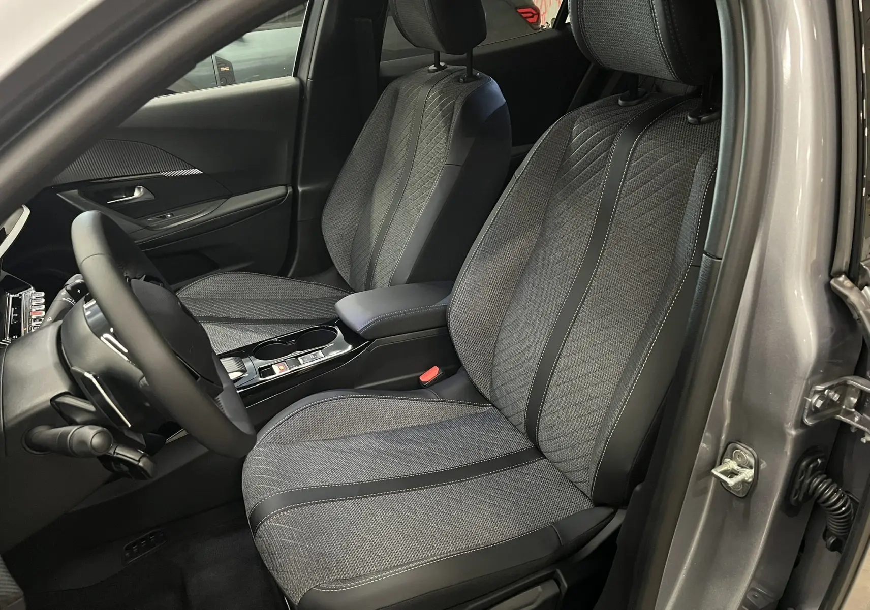 Vue intérieure côté conducteur du Peugeot 2008 gris Artense, mettant en valeur les sièges tissu et cuir noir au design moderne.