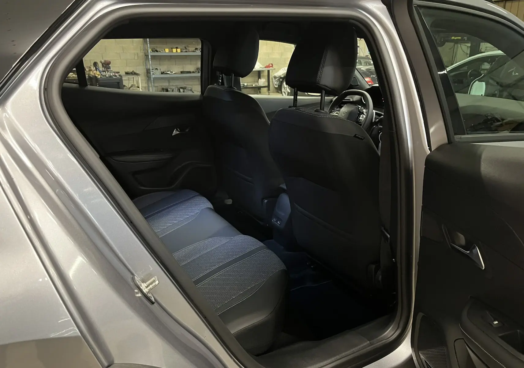 Vue intérieure arrière droite du Peugeot 2008 gris Artense, montrant les sièges en tissu et cuir noir avec détails bleutés.